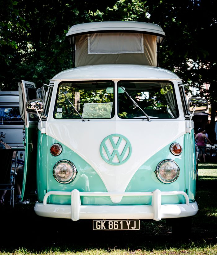 Front view of a vintage mint VW camper van at a camping site, ideal for travel and retro adventures.