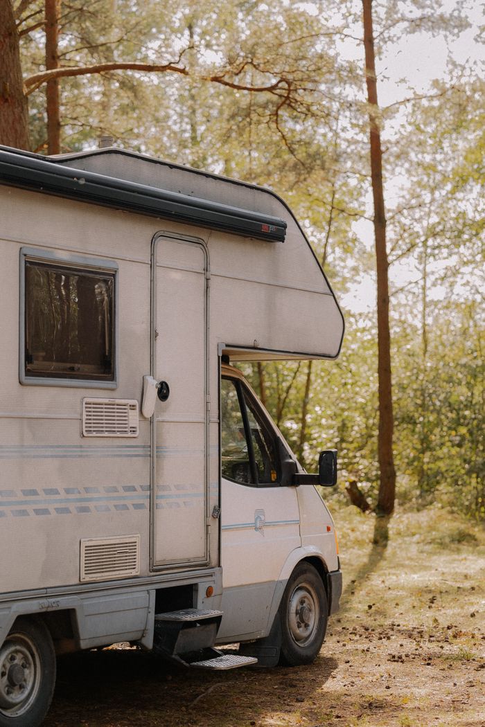 A serene image of a camper van parked in a sunlit forest, ideal for travel and adventure themes.