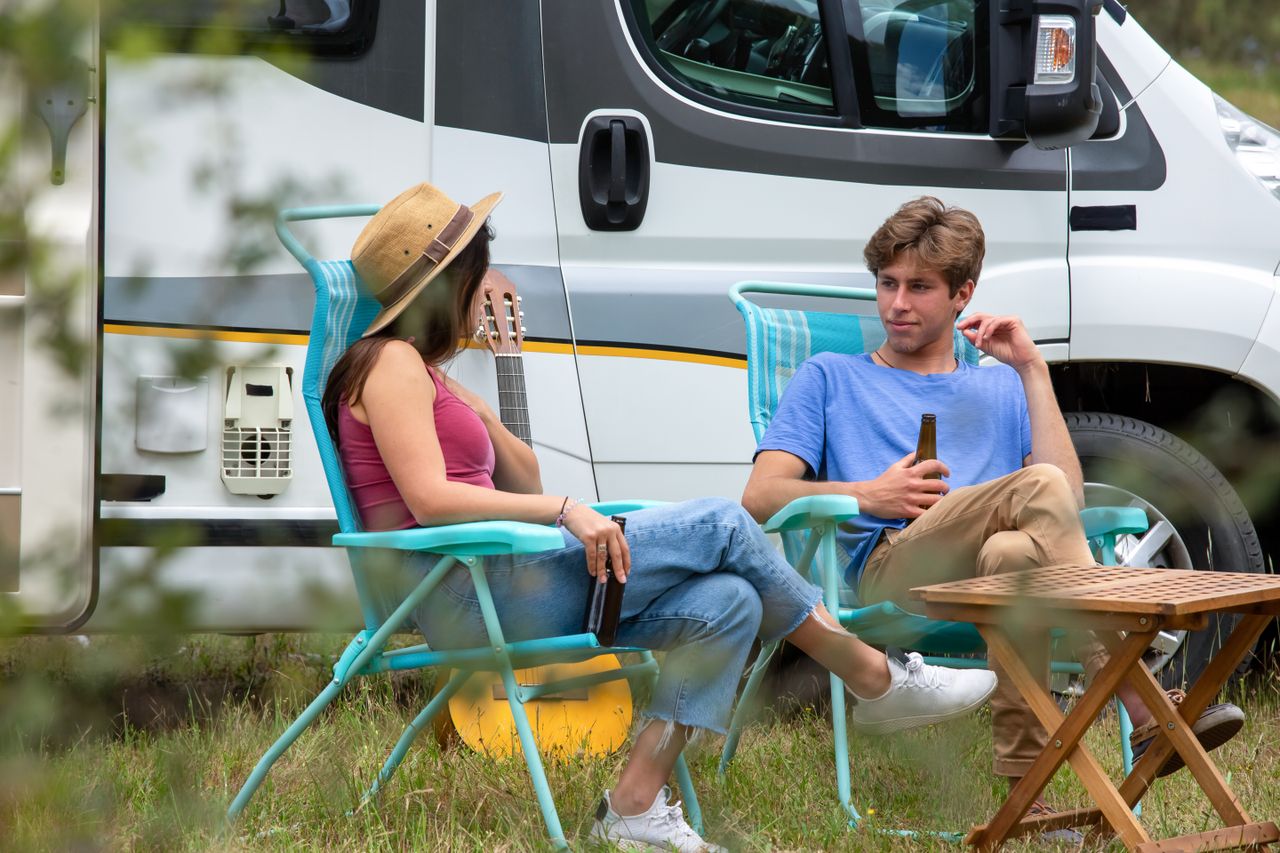 A young couple enjoys leisure time outside their camper van, embodying a carefree outdoor lifestyle.